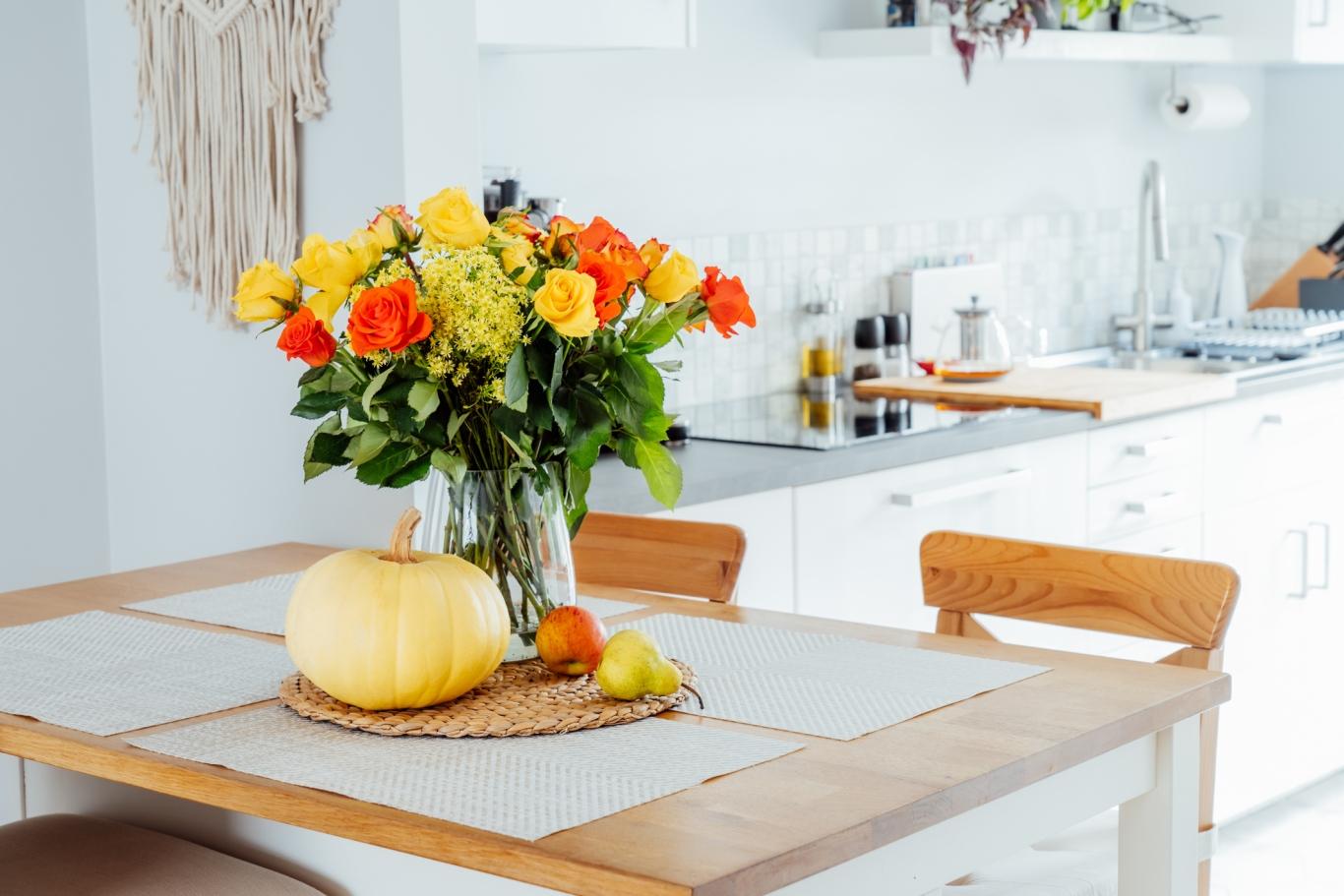 A small kitchen table adorned with fall flowers and pumpkins.