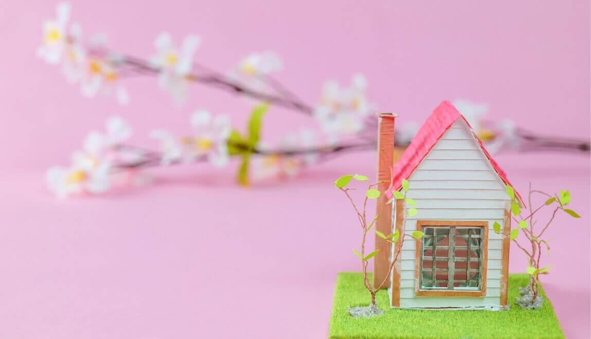 Miniature craft house with a branch of spring flowers resting behind it