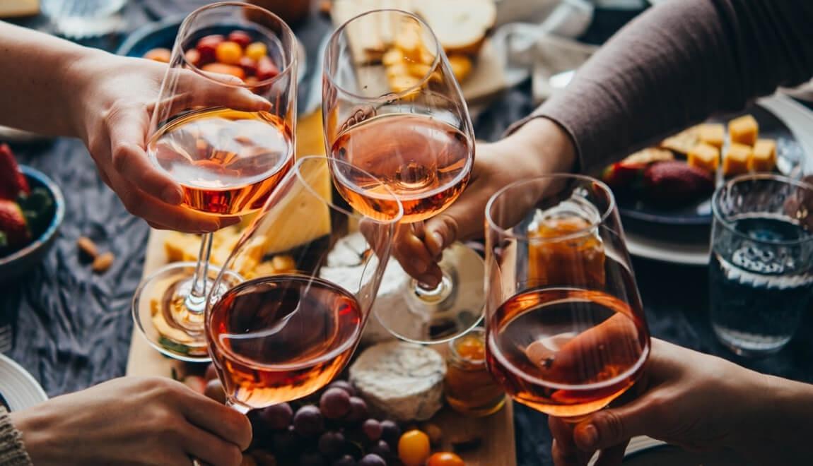 Glasses of wine being clinked together over a dinner table.