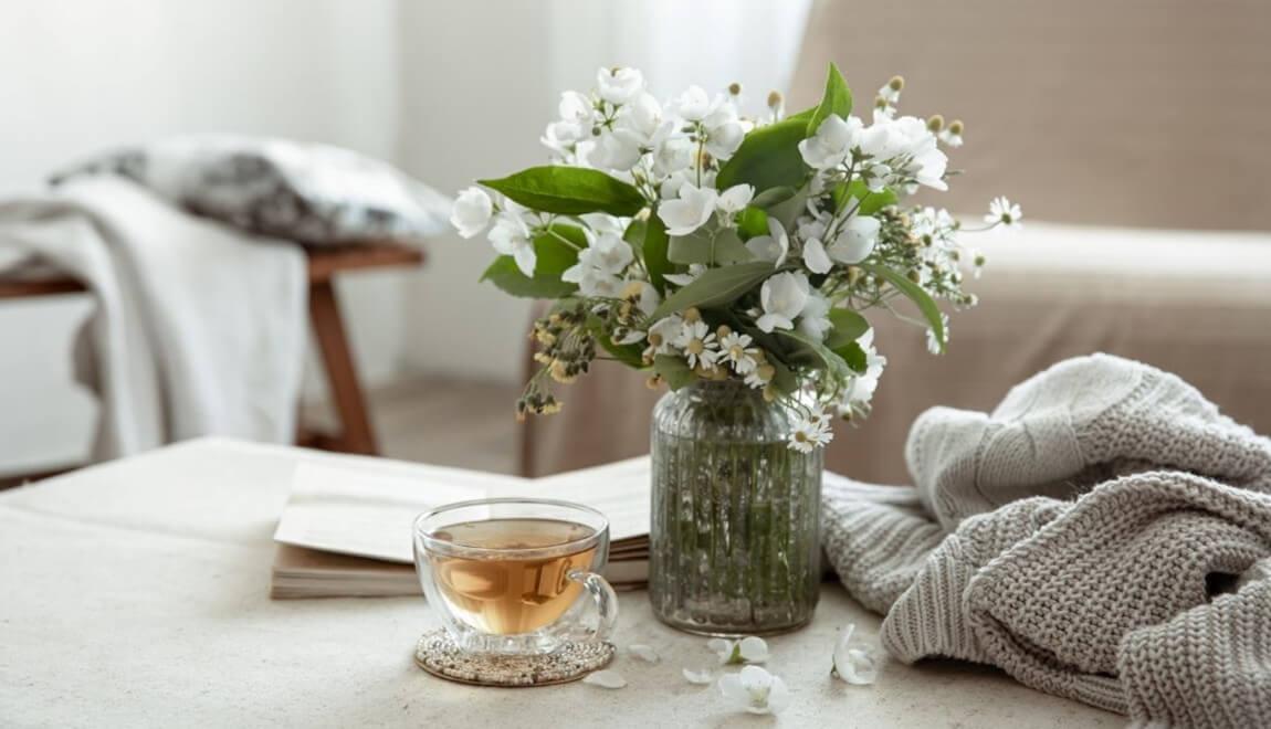 A table with a vase of flowers, cup of tea, and cozy grey sweater