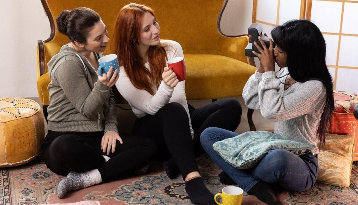 Three women sitting on the living room floor taking photos.