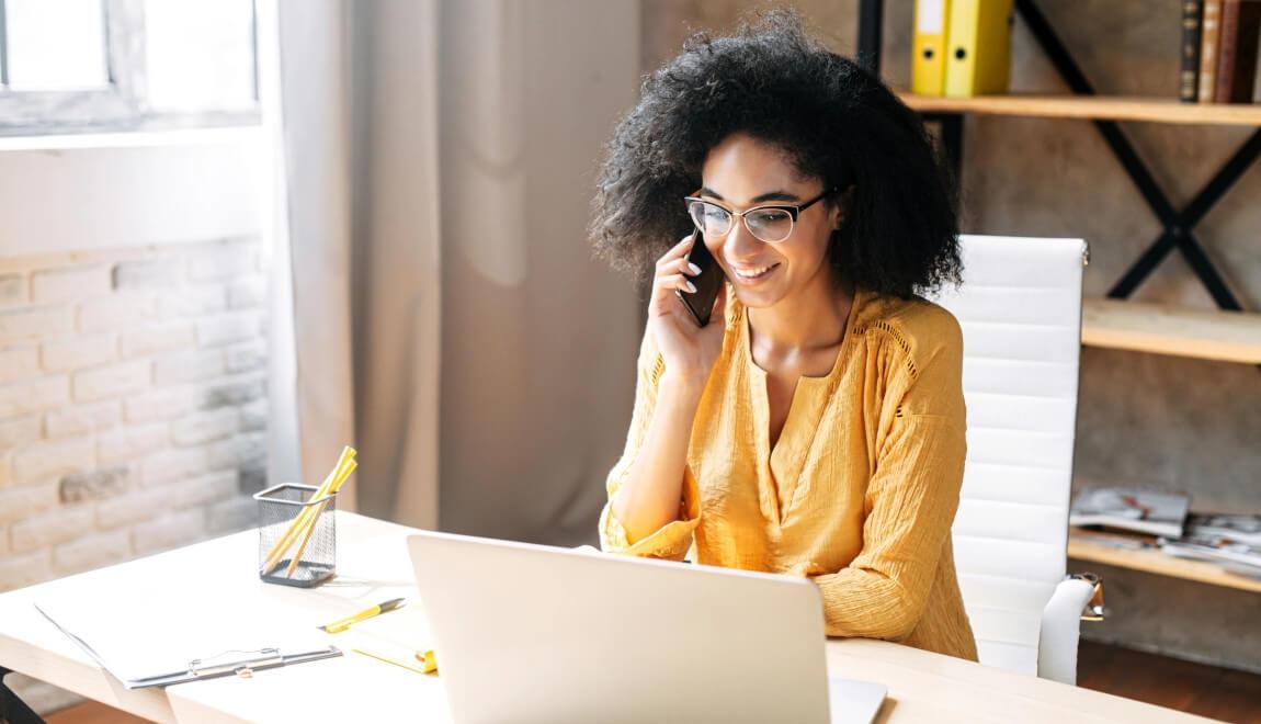 A woman sits at a desk and talks on the phone. 