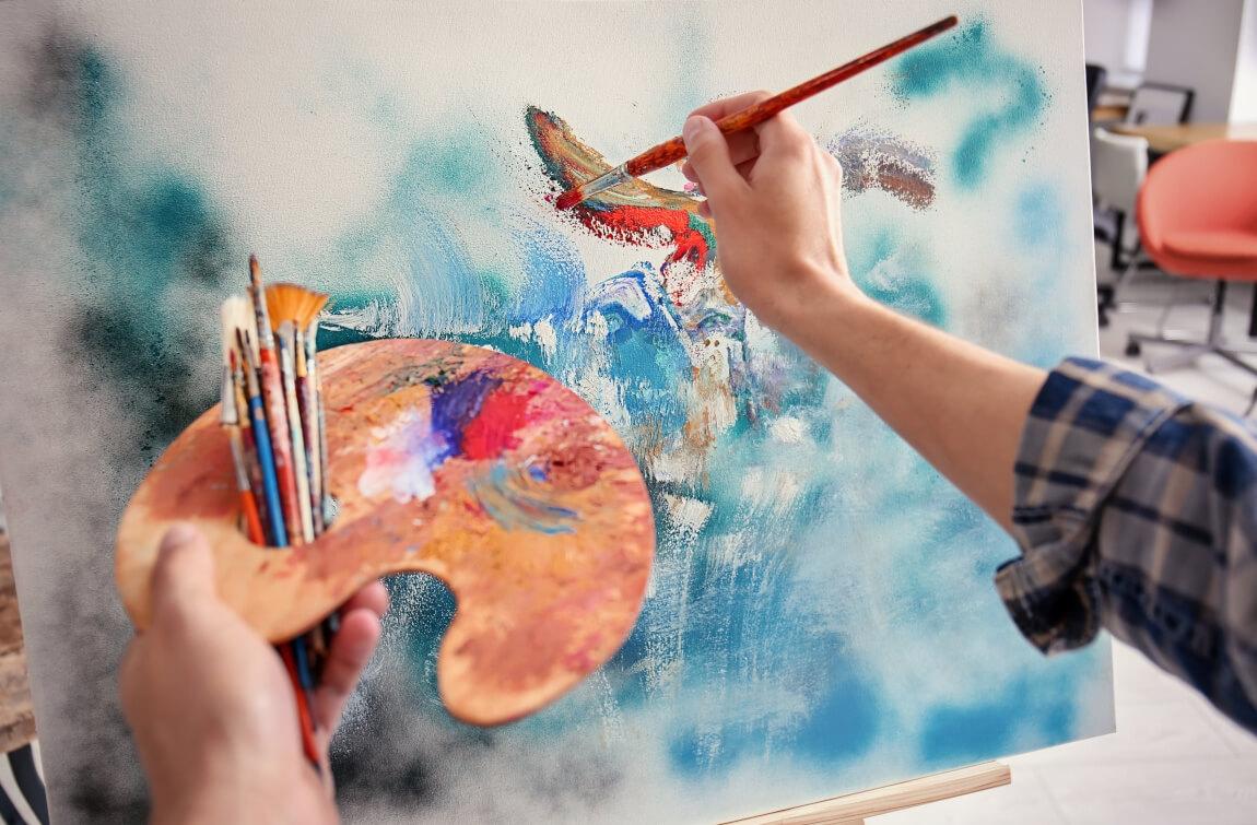 An image of a person painting on a canvas with a paint brush in their hand. 