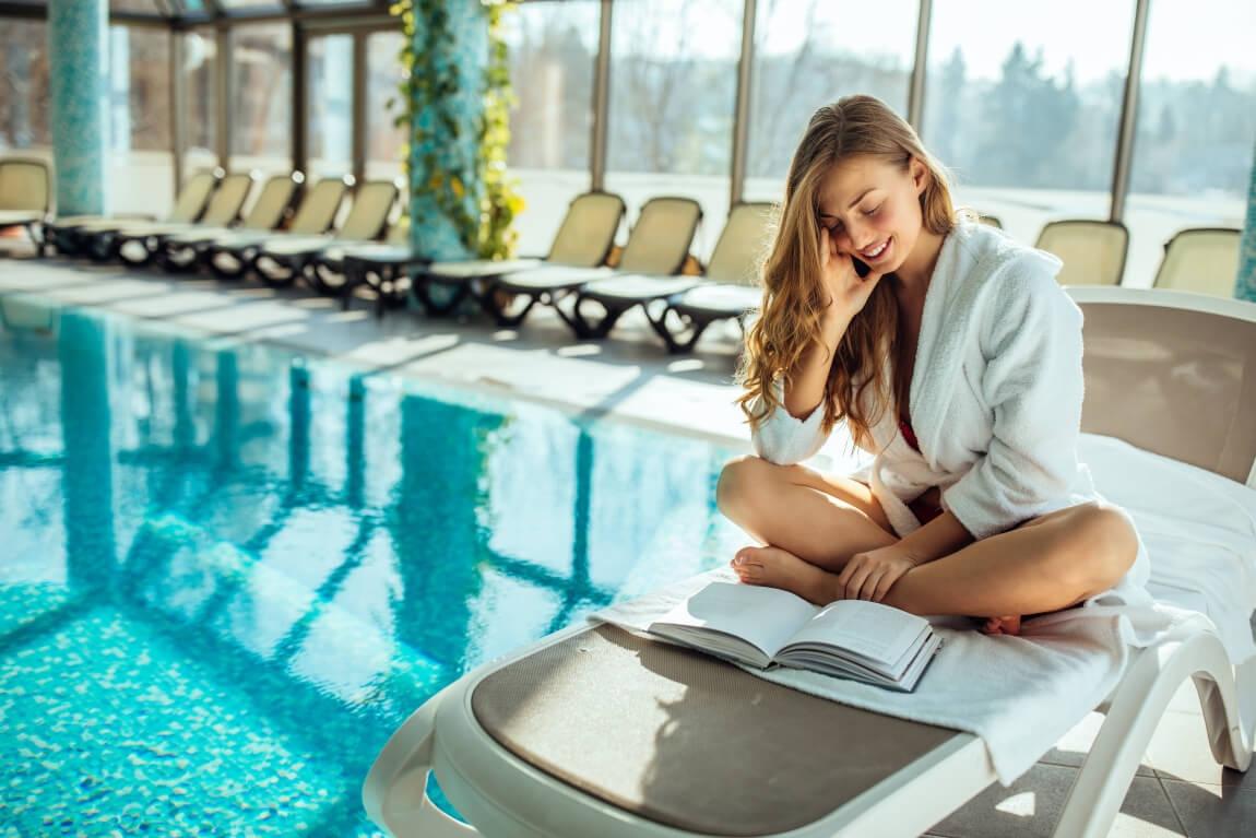 An image of a women sitting on a lounge chair next to a pool. 