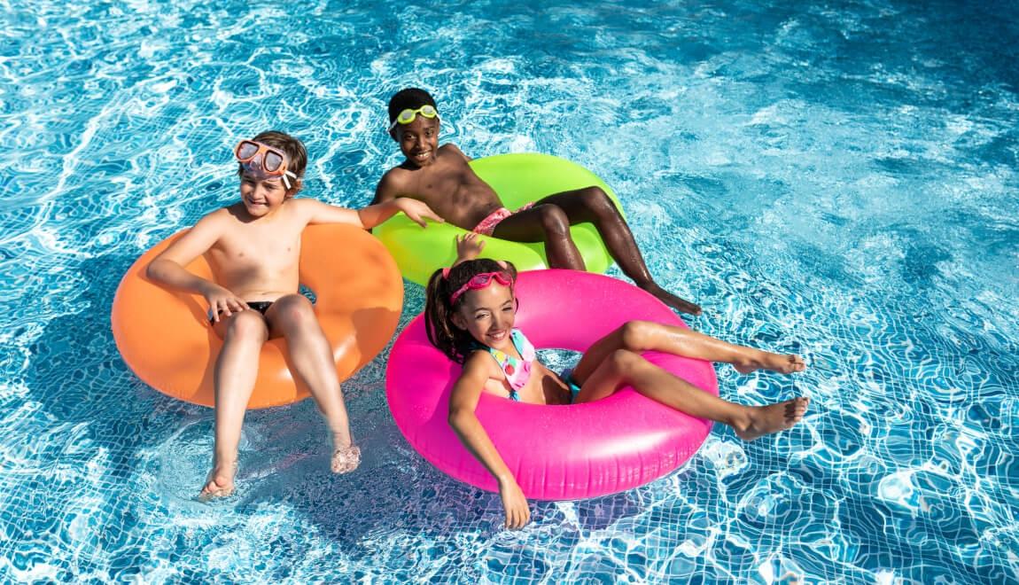 An image of three children sitting on innertubes in a pool.