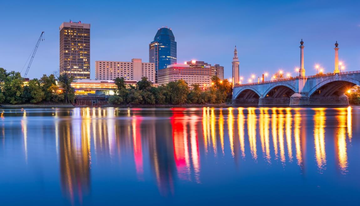 City lights reflect on the water's surface at dusk.