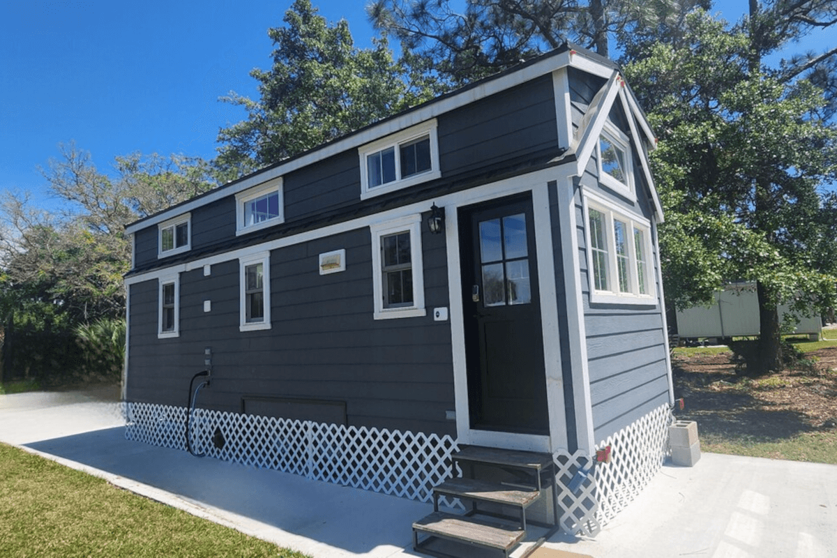 A blue barndominium-style tiny home sits in a grassy field in Cocoa, Florida.