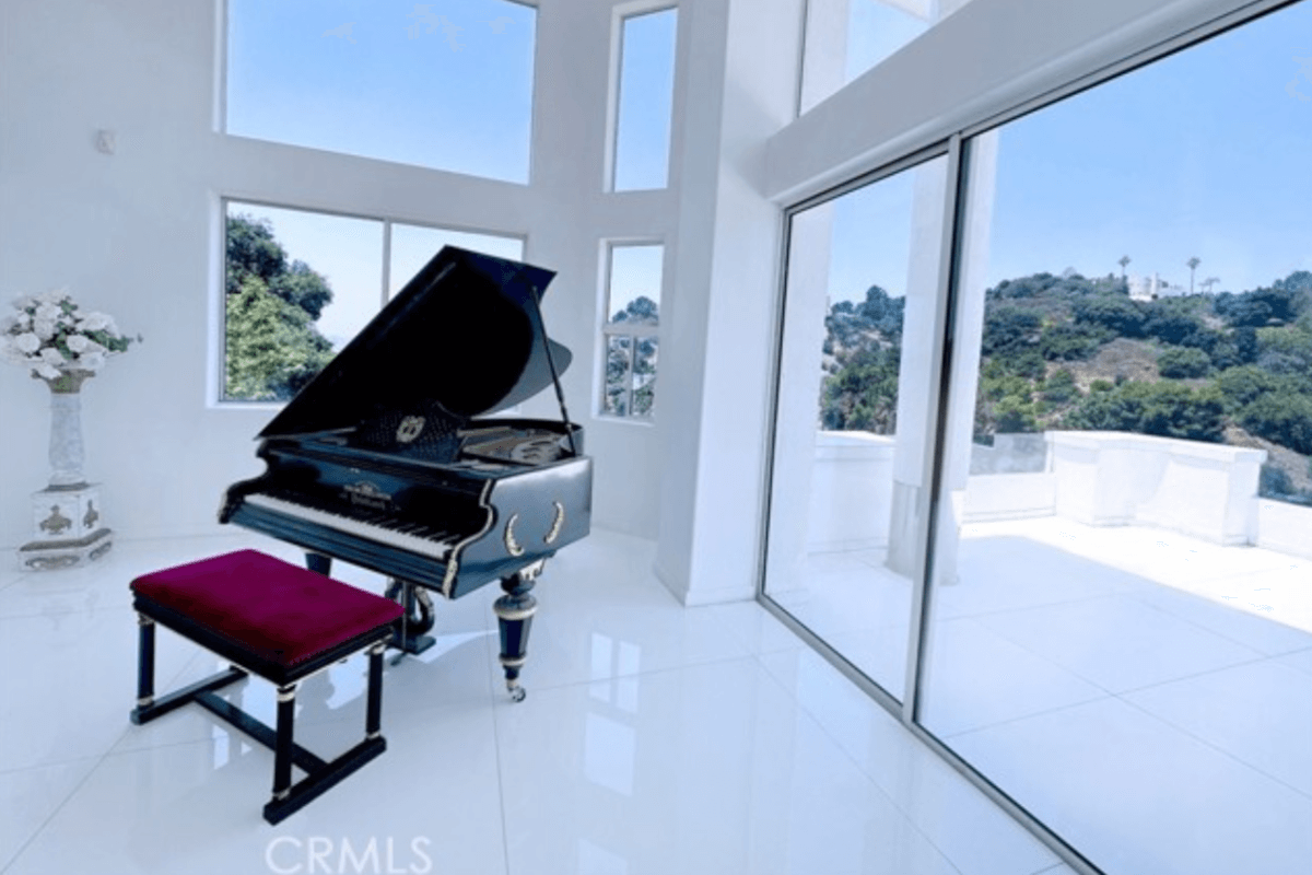 An ornate grand piano sits by a window looking out at the mountains.