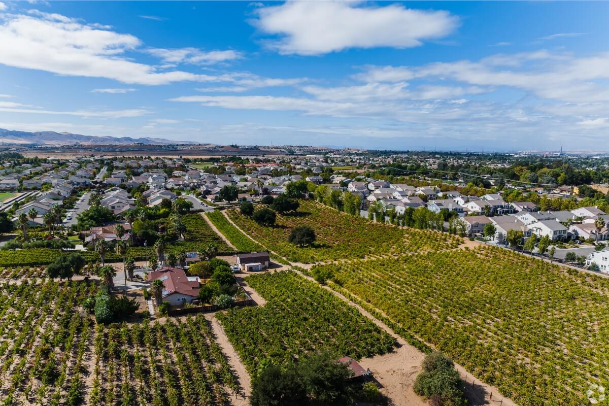 An aerial view of Brentwood, California, shows a vineyard in the foreground and mountains on the horizon.