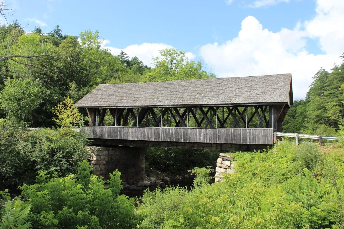 Packard Hill Covered Bridge overlooks the Mascoma River and is surrounded by lush greenery.