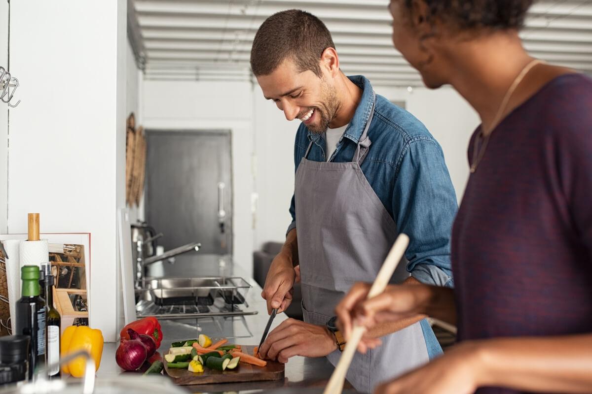 A young couple smiles while cooking together.