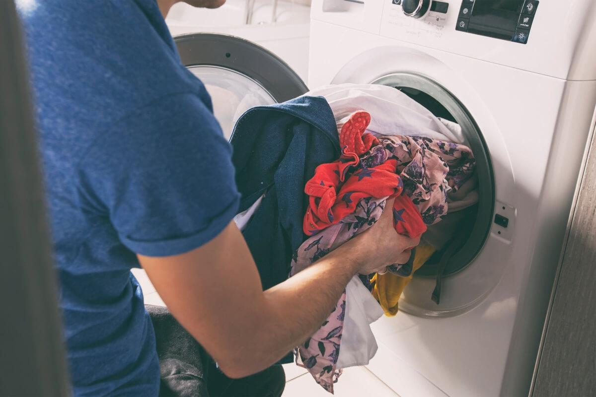 A young man loads a dryer with freshly cleaned clothes.