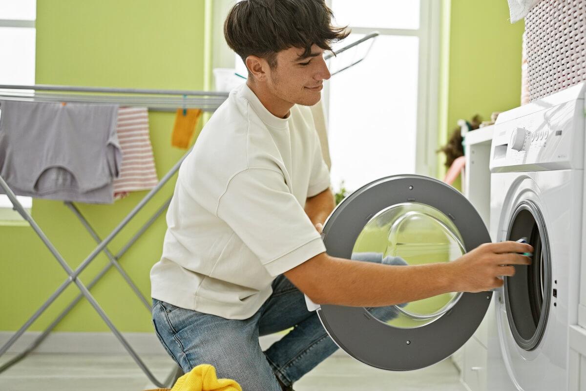 A young man tosses a laundry detergent pod into a washing machine.