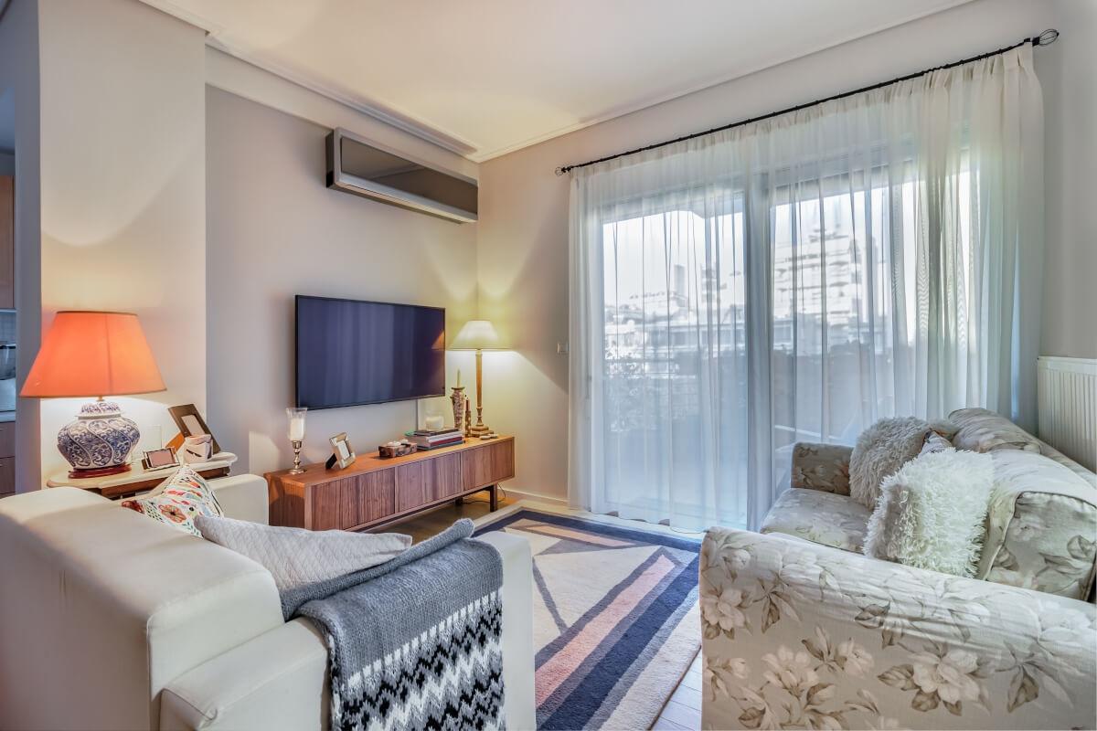 A small apartment living room has two couches and a TV next to a floor-to-ceiling window.