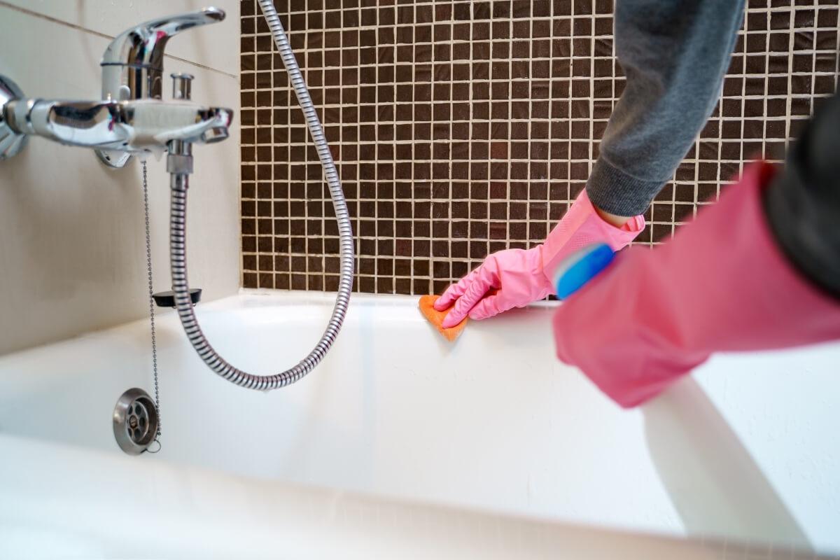 A person wearing pink cleaning gloves scrubs at a bathtub.