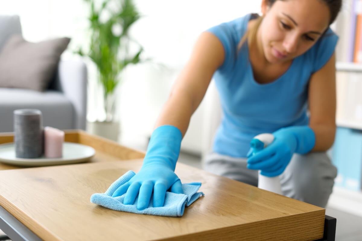 A woman cleans a wooden coffee table with a microfiber towel.