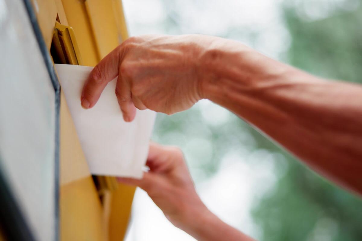 Human hand putting letter into yellow mailbox.