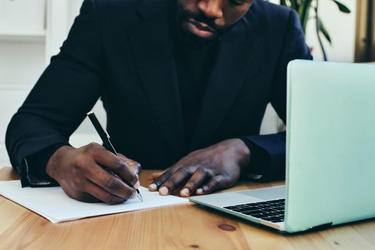 Man writing letter next to laptop.