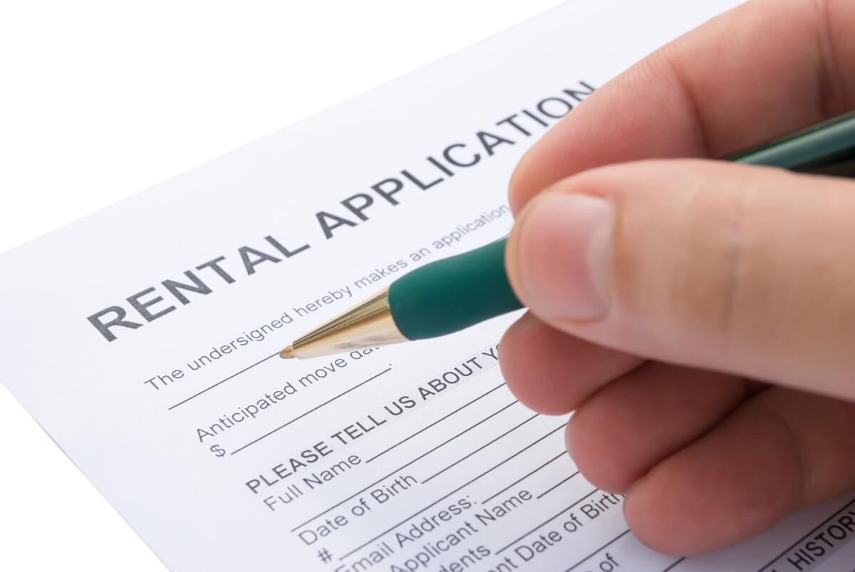 Hand holding pen filling out a rental application.
