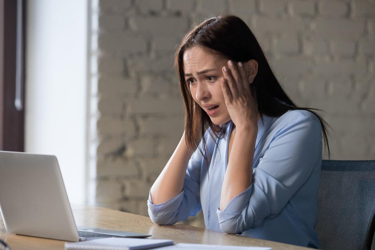 A distressed woman looks at something on her laptop.