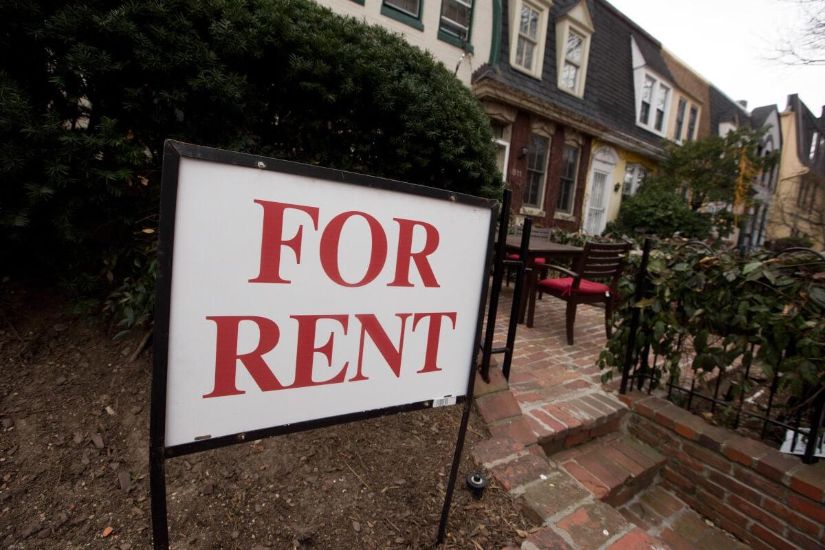 A "For Rent" sign stands in front of old brick row houses.