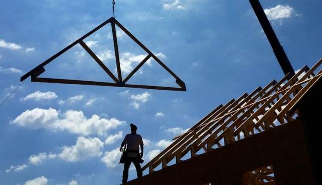 Housing support suspended by a crane being lowered onto an unfinished roof.