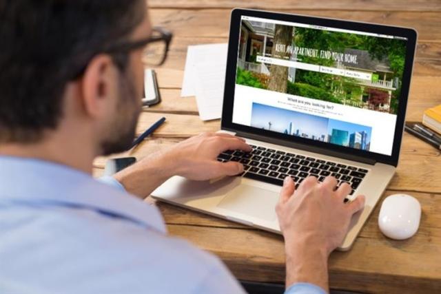 A man with glasses searches for apartments on his laptop.