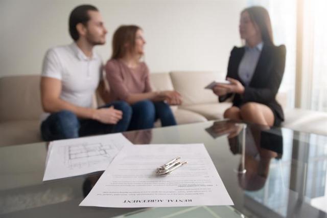 Lease agreement on table in front of a couple talking to a rental agent.