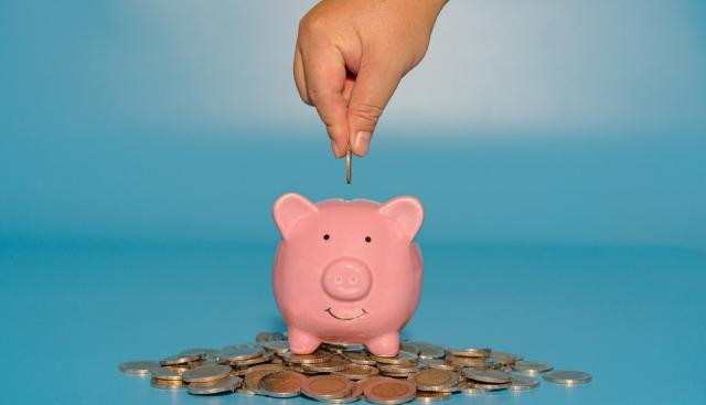 A hand dropping a coin into a pink piggy bank.