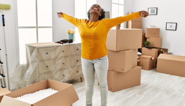 A happy woman stands in her new apartment, arms outstretched.