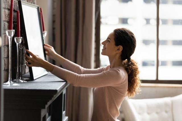 A woman places a picture on the mantel of a fireplace.