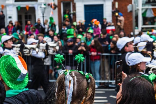 A crowd dressed in St. Patrick’s Day gear watches a parade pass by.