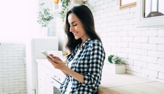 A woman standing in a white kitchen looking at her phone.