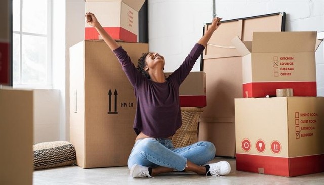 Woman sitting on the floor with raised arms, surrounded by boxes.