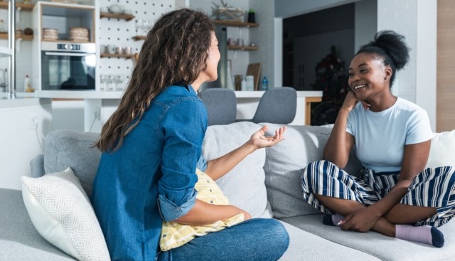 Two roommates having a conversation,while sitting on the couch.