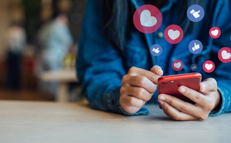 A person on their phone with hearts and likes emojis floating above the screen