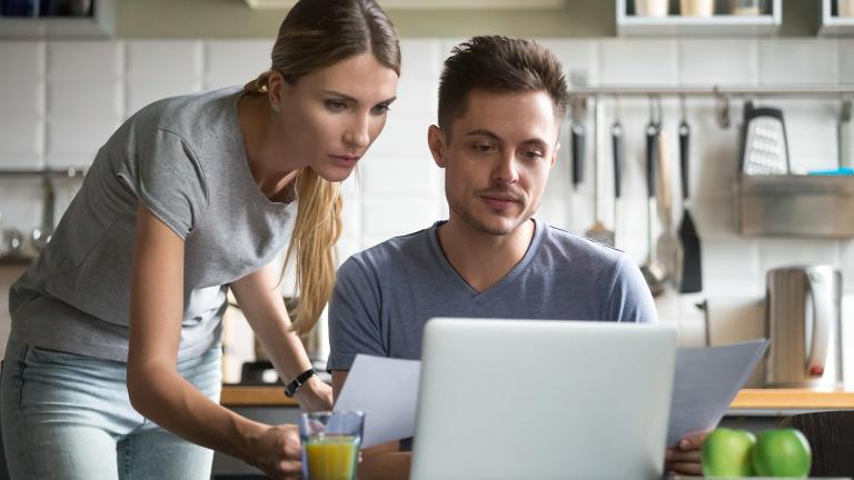 A couple comparing their documents to their laptop