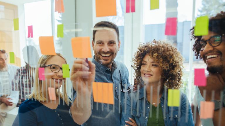 Team brainstorms ideas on glass wall with post-it notes