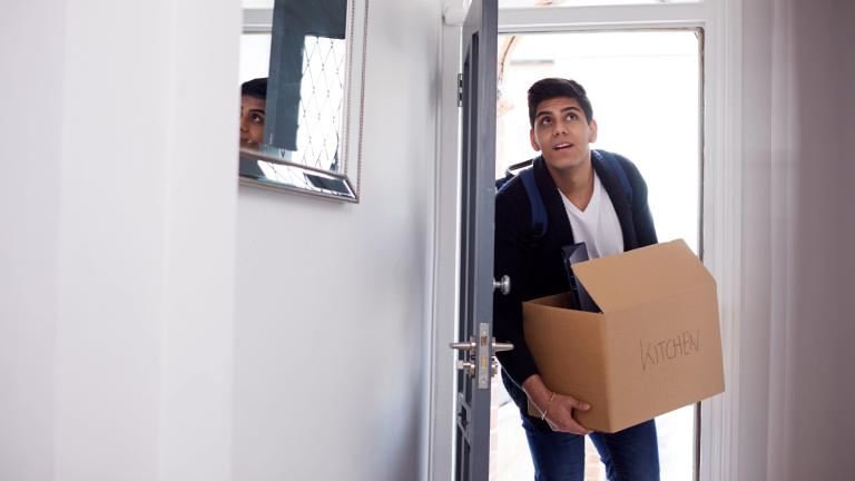 Male college student steps into apartment carrying a box