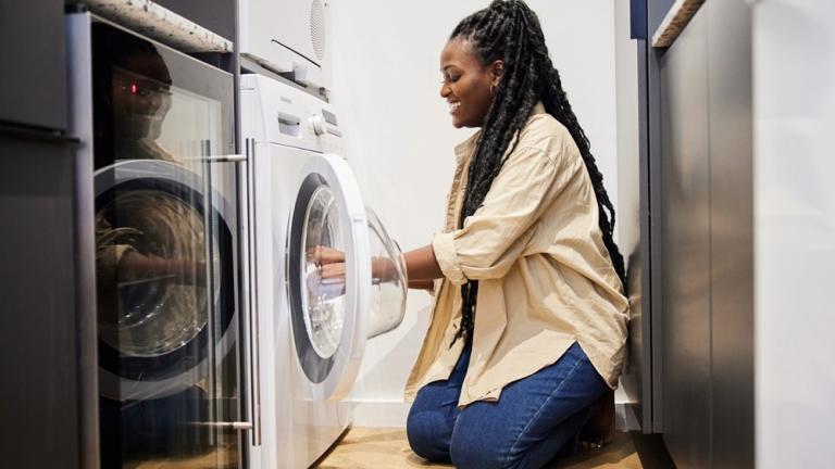 Woman kneels in kitchen to load washing machine