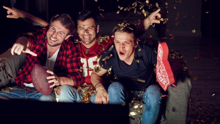 Group of male friends cheer while watching football on TV