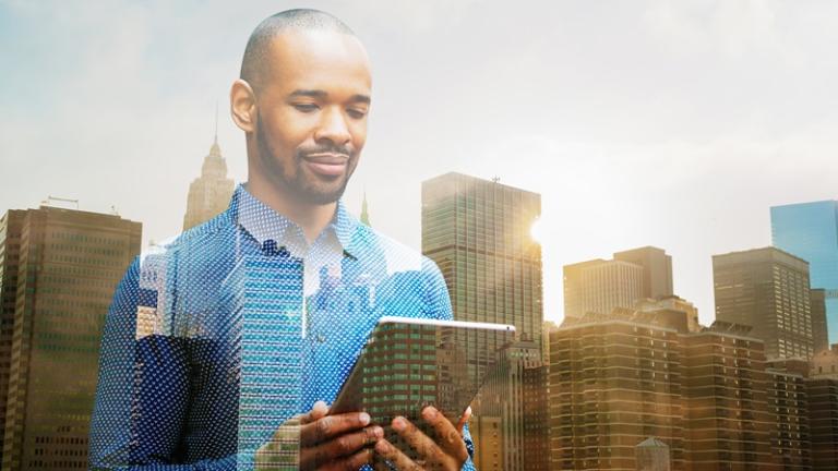 Businessman looks at tablet with high-rise buildings behind him