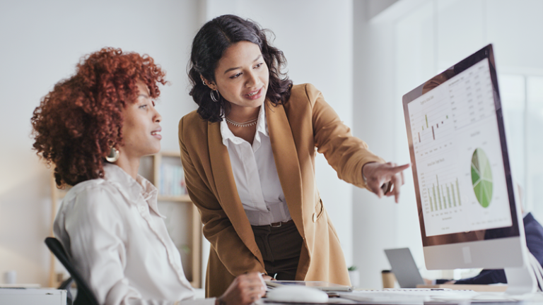 Woman points to computer screen in conversation with colleague