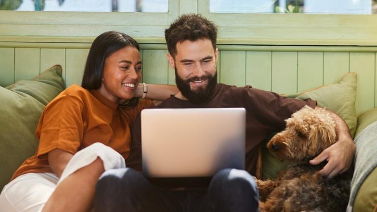 Couple with dog looking at laptop together on the couch