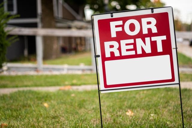 A for rent sign placed in the grassy yard of a vacant property