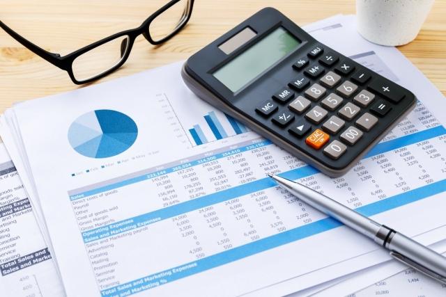 A printout of tables and graphs with adjacent reading glasses, calculator, and a pen