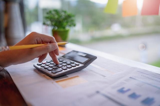 An image of a person's hand holding pencil while typing numbers in on a calculator. 