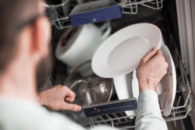 A man places a dirty plate in a dishwasher.