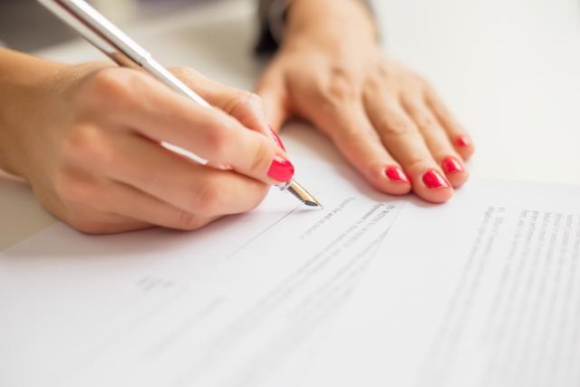 Woman is sigining a contract with a pen.