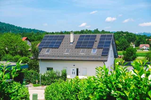 White house with solar panels on roof is surrounded by plants.